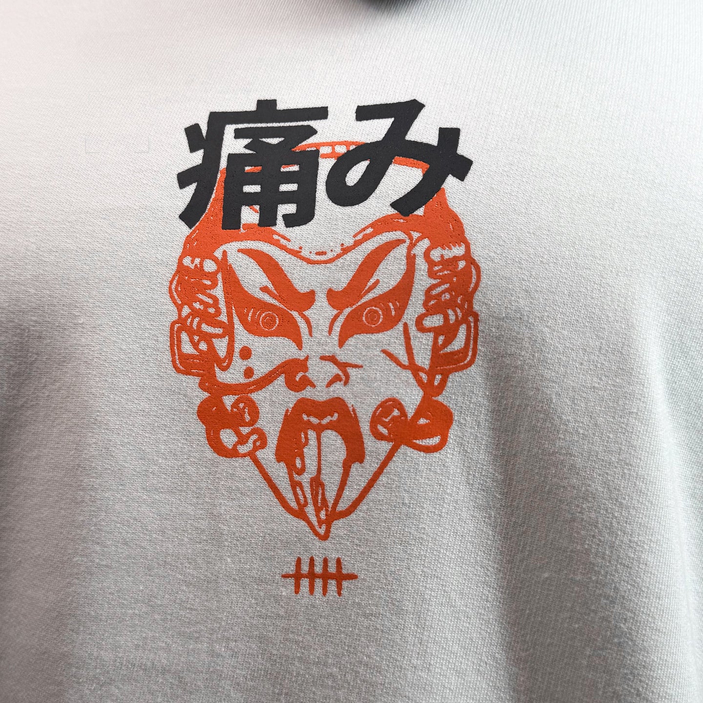 A close-up of a white crewneck sweatshirt featuring a graphic print of a red and black mask with Japanese characters, shown on a model wearing a black respirator mask.
