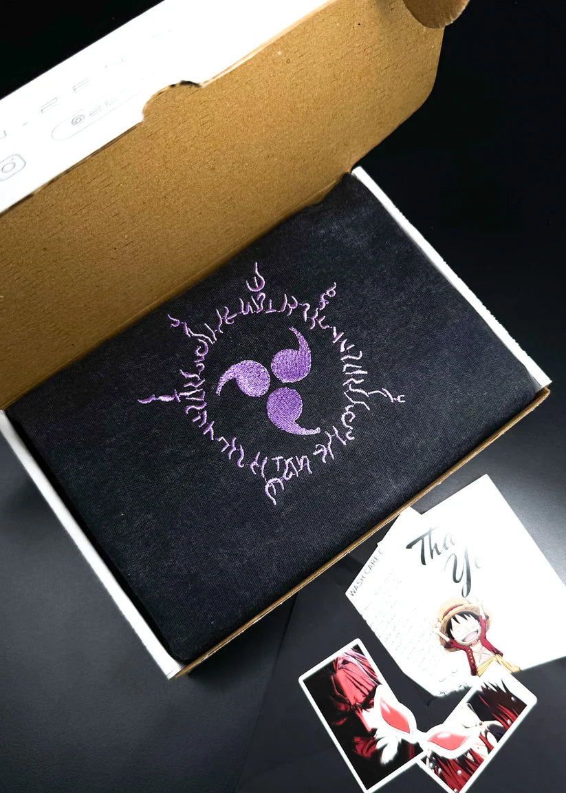 Black notebook with purple triskelion design and text, open to reveal a white card with illustrations.